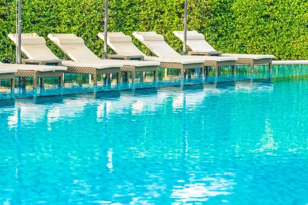 Poolside lounge chairs with greenery backdrop, reflecting on calm water. -pool and decks