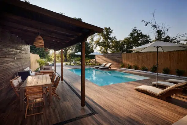 Modern backyard pool with wooden deck, shaded seating, and umbrellas. -pool and decks