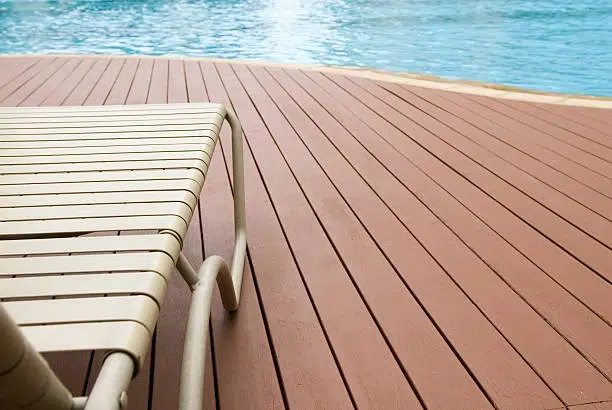 Wooden pool deck with a lounge chair beside the water. -swimming pool and deck