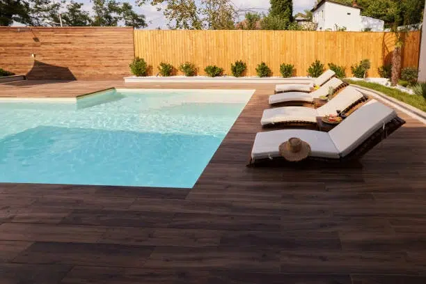 Poolside area with wooden deck, sun loungers, and privacy fence. -swimming pool and deck