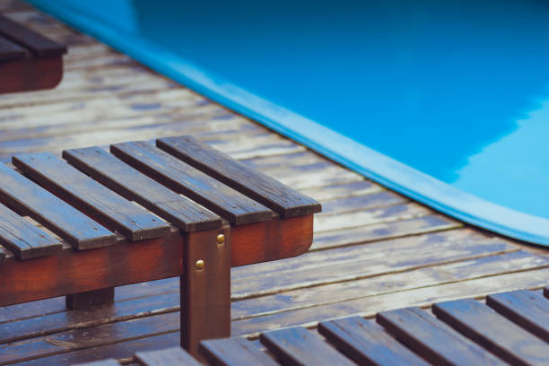 Close-up of a wooden deck with lounge chairs next to a pool. -swimming pool and deck